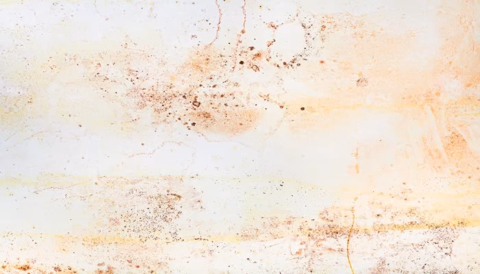 Superficie desgastada presenta manchas oxidadas y decoloraciones. La textura es rugosa, mostrando grietas y tonos marrones y beige. El entorno sugiere deterioro y paso del tiempo.