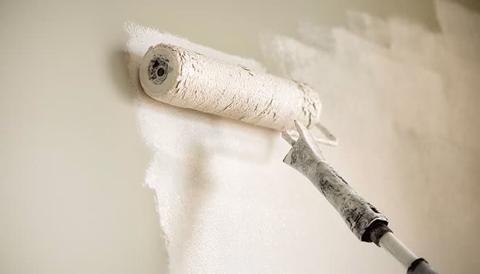 Un rodillo de pintura aplica pintura blanca sobre una pared; se extiende uniformemente, cubriendo parcialmente el color anterior en un entorno interior.