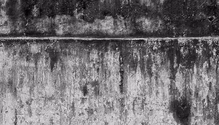 Una pared de concreto muestra manchas oscuras y marcas de desgaste, evocando abandono en un entorno posiblemente industrial, sin presencia de texto u otros elementos distintivos.
