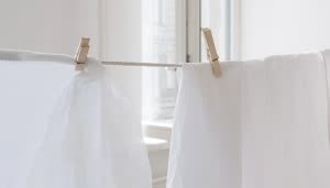 Dos pinzas de madera cuelgan ropa blanca en una cuerda, iluminada por luz natural, cerca de una ventana en un interior.