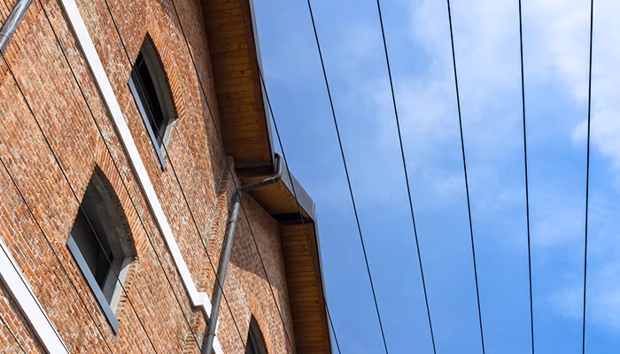 Edificio de ladrillo con ventanas arqueadas, inclinado hacia la izquierda. Varios cables eléctricos cruzan el cielo azul despejado en el lado derecho.