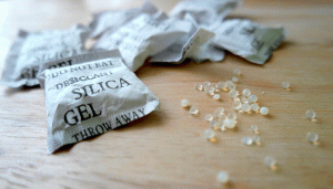 Bolsitas de gel de sílice, colocadas sobre una superficie de madera, con texto "DO NOT EAT," "DESICCANT," "SILICA GEL," "THROW AWAY" y algunas perlas desecantes dispersas alrededor.