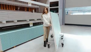 Una persona empuja un carrito con una gran placa de yeso en una tienda de construcción, rodeada de estantes con más placas apiladas.