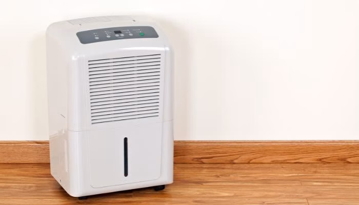 Un deshumidificador blanco está quieto sobre un suelo de madera, junto a una pared clara. Su panel de control digital está visible en la parte superior.