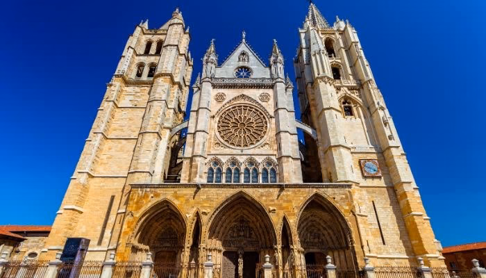 Catedral gótica de León. Imponente, elevándose hacia el cielo, con una fachada detallada y rosetón central. Flanqueada por dos torres simétricas, bajo un cielo despejado.